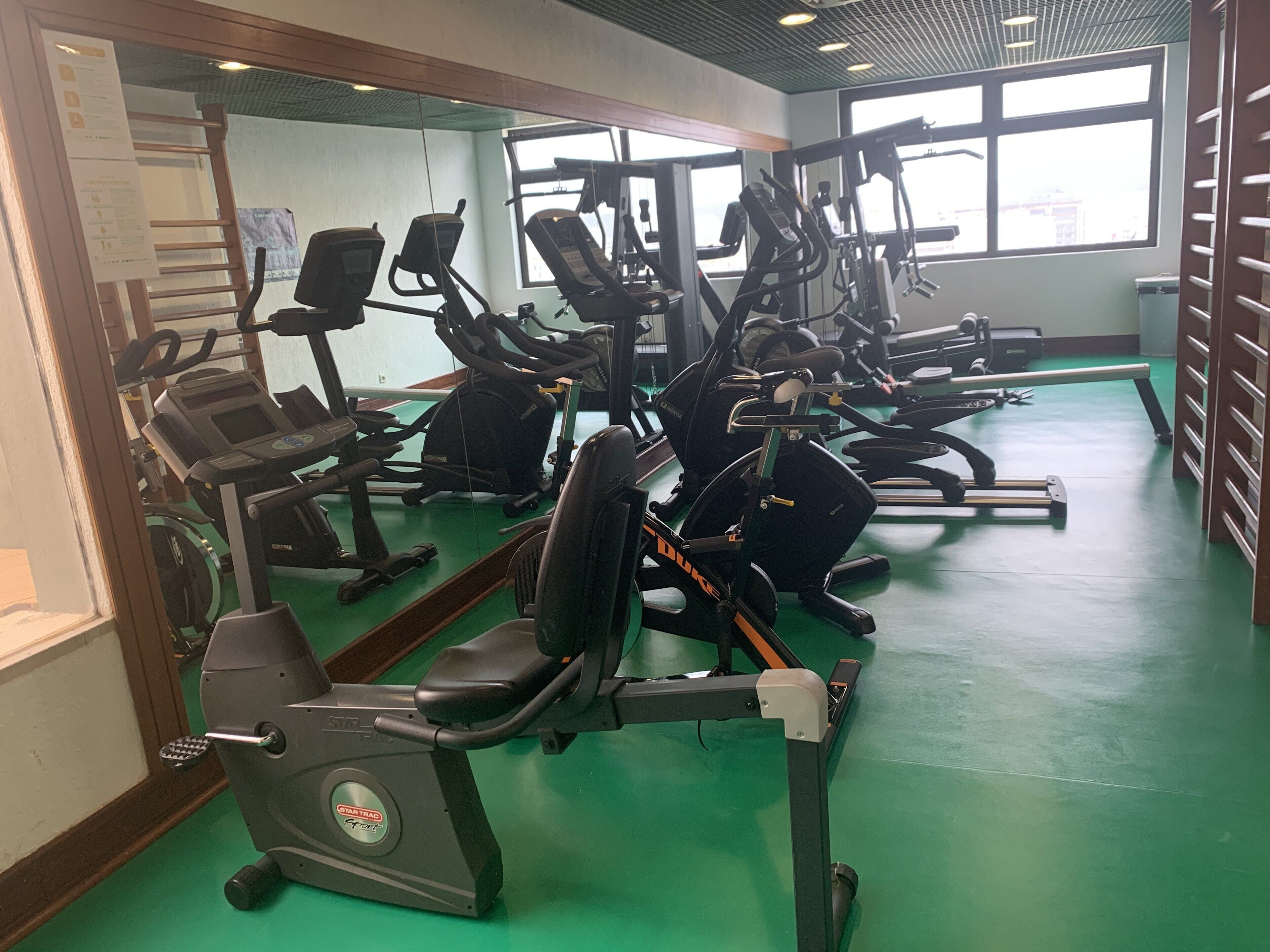 Un gimnasio con varias máquinas de ejercicio, incluyendo cintas de correr y elípticas, dispuestas en filas.