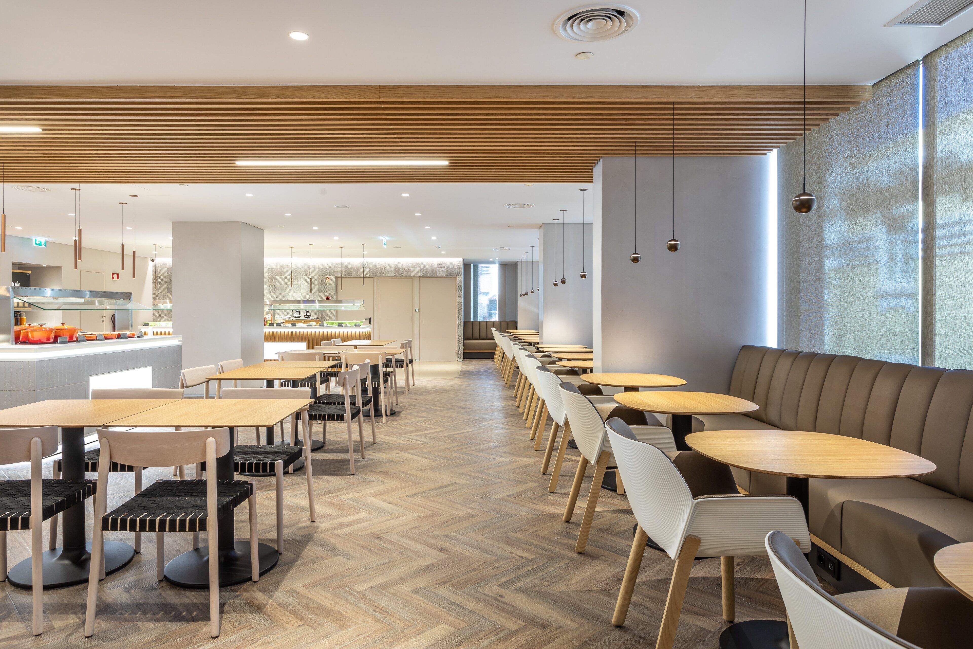 Un comedor moderno con mesas y sillas de madera, suelo con patrón de espiga y lámparas colgantes.
