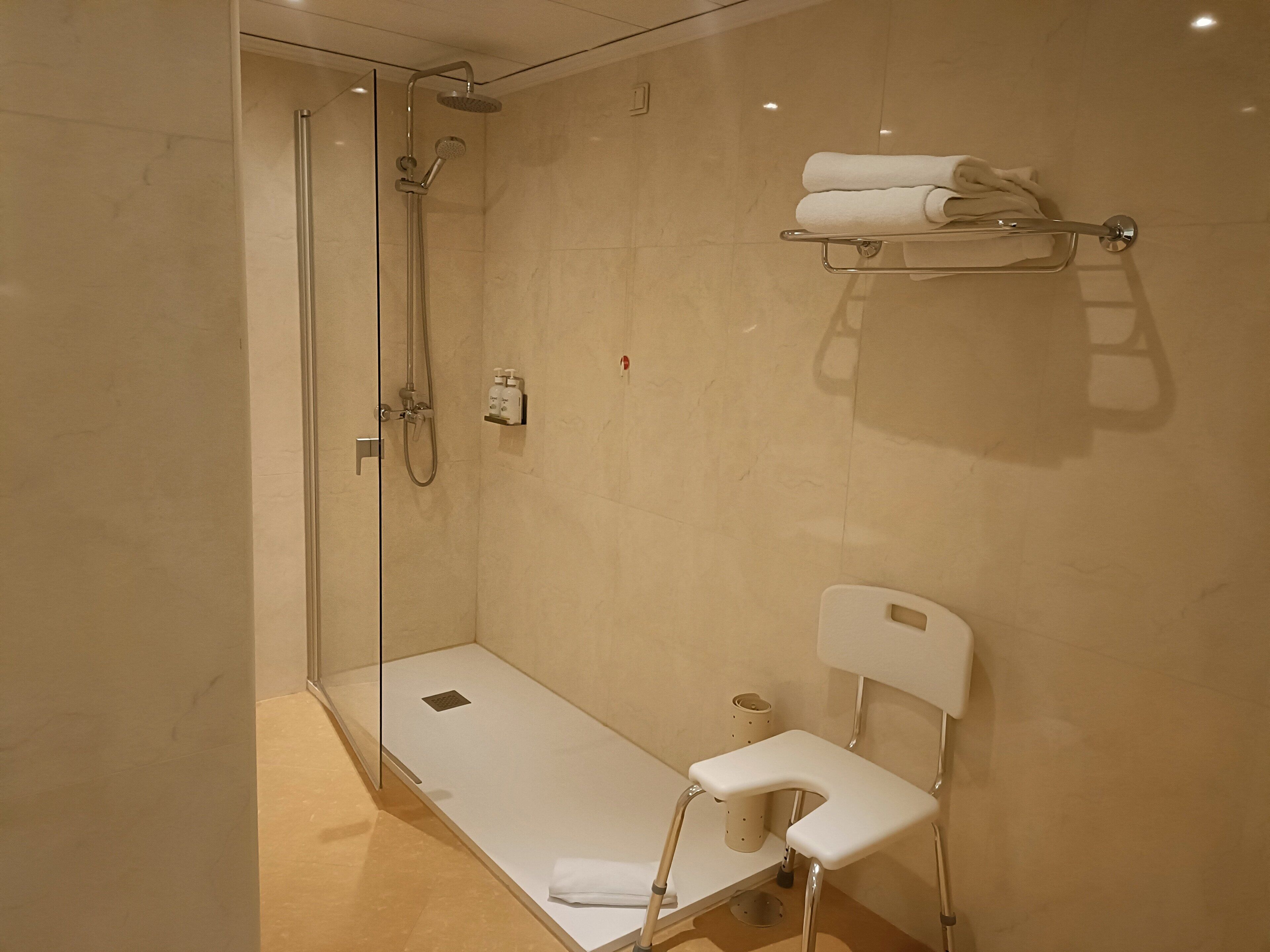 A modern bathroom with a walk-in shower, a toilet with a safety seat, and a towel rack.