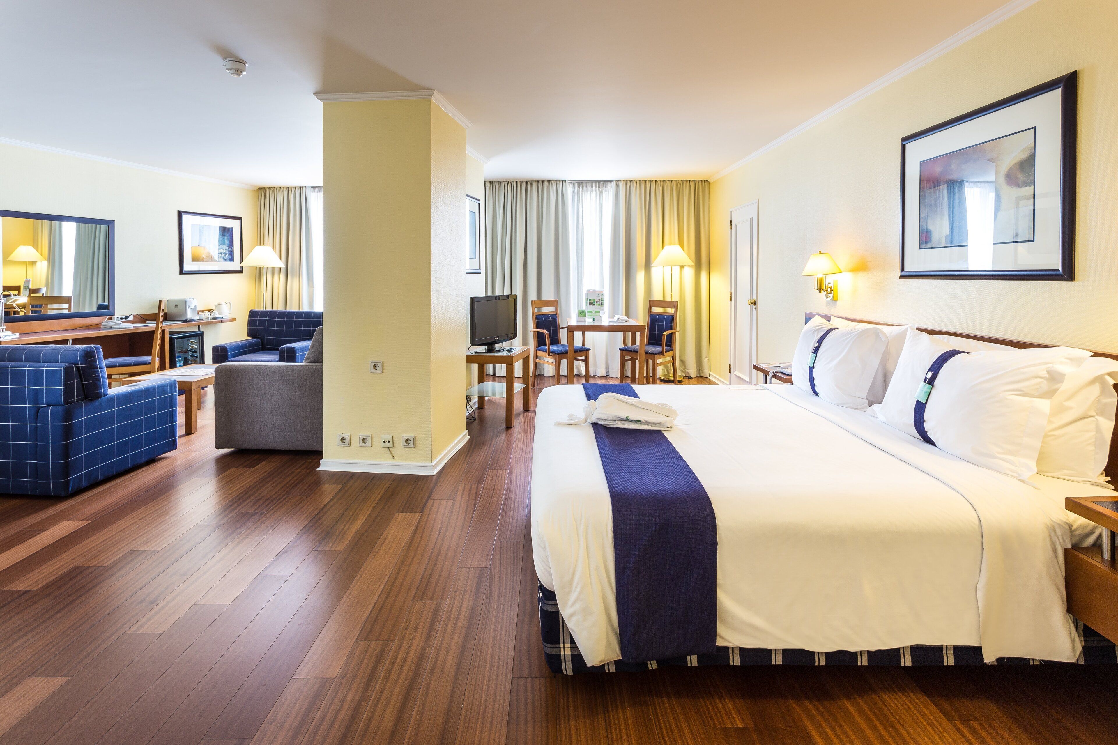 Ein Hotelzimmer mit einem großen Bett, einem Schreibtisch mit Computer, einem Fernseher und einer Sitzecke mit zwei Stühlen und einem Tisch.