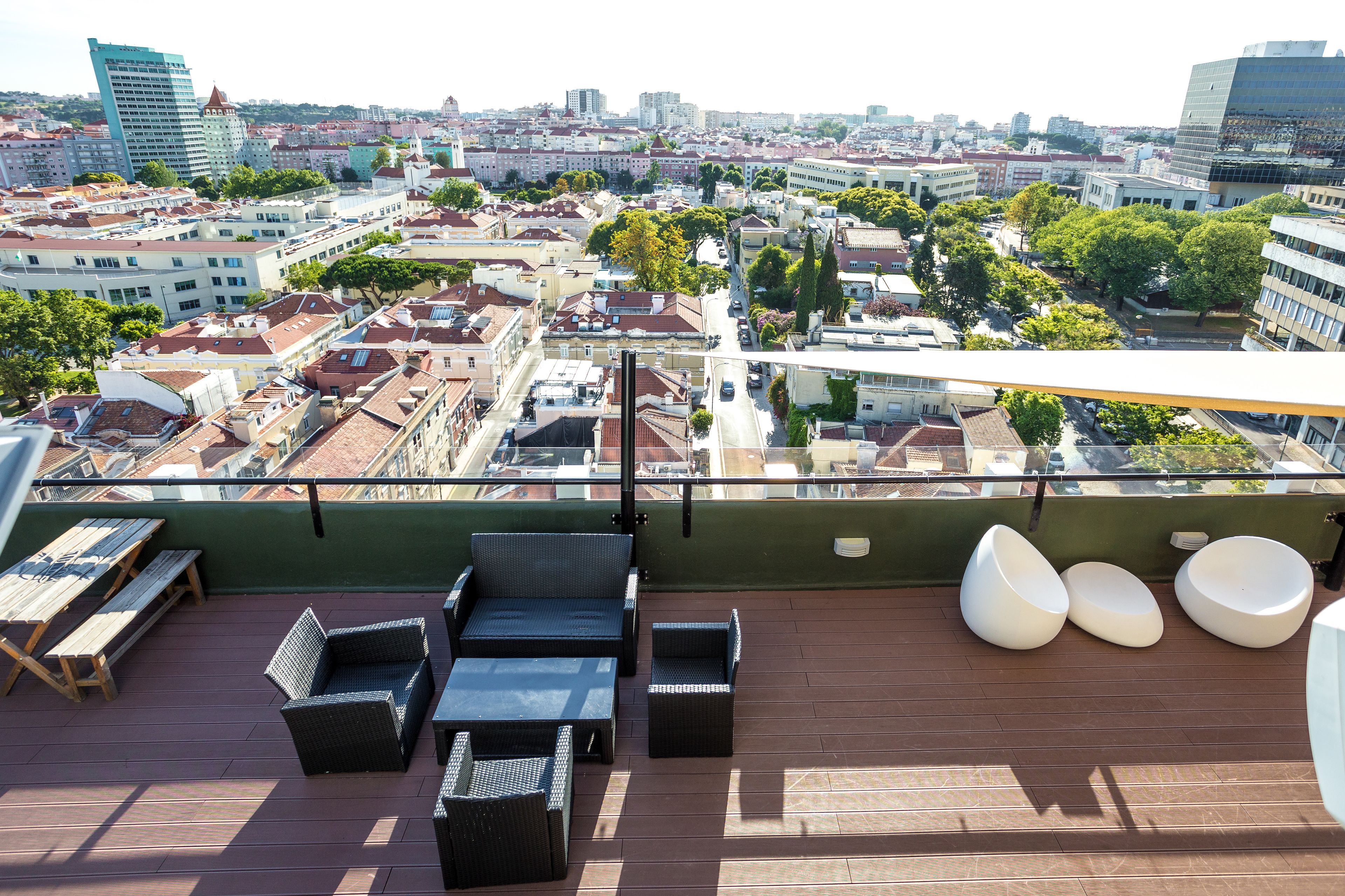 A rooftop terrace with wicker furniture, a table, and a view of a cityscape.