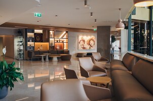 Um lobby moderno com áreas de estar, um café e uma grande pintura abstrata na parede.