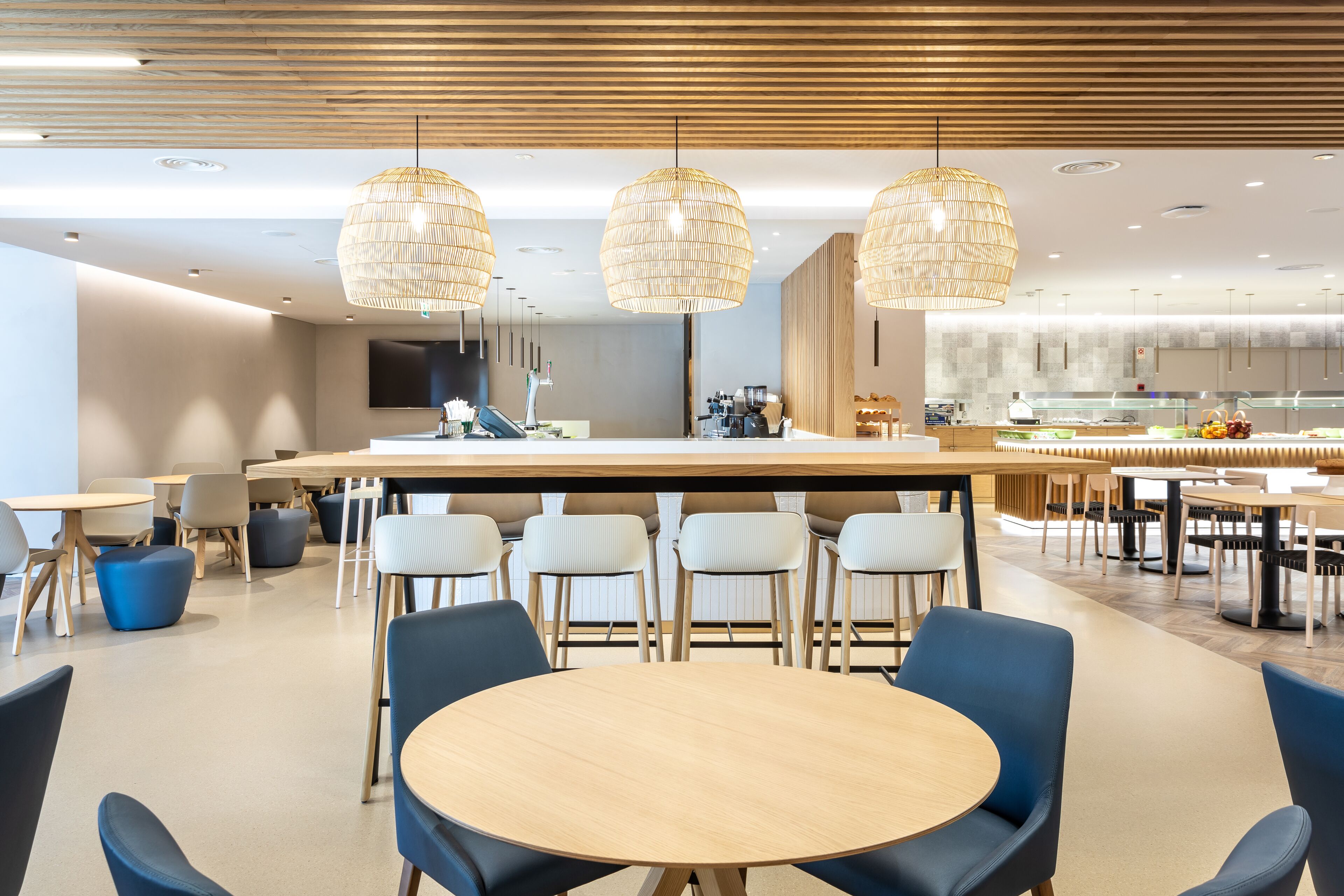A modern dining area with round tables and blue chairs, a central bar area, and hanging wicker lamps.