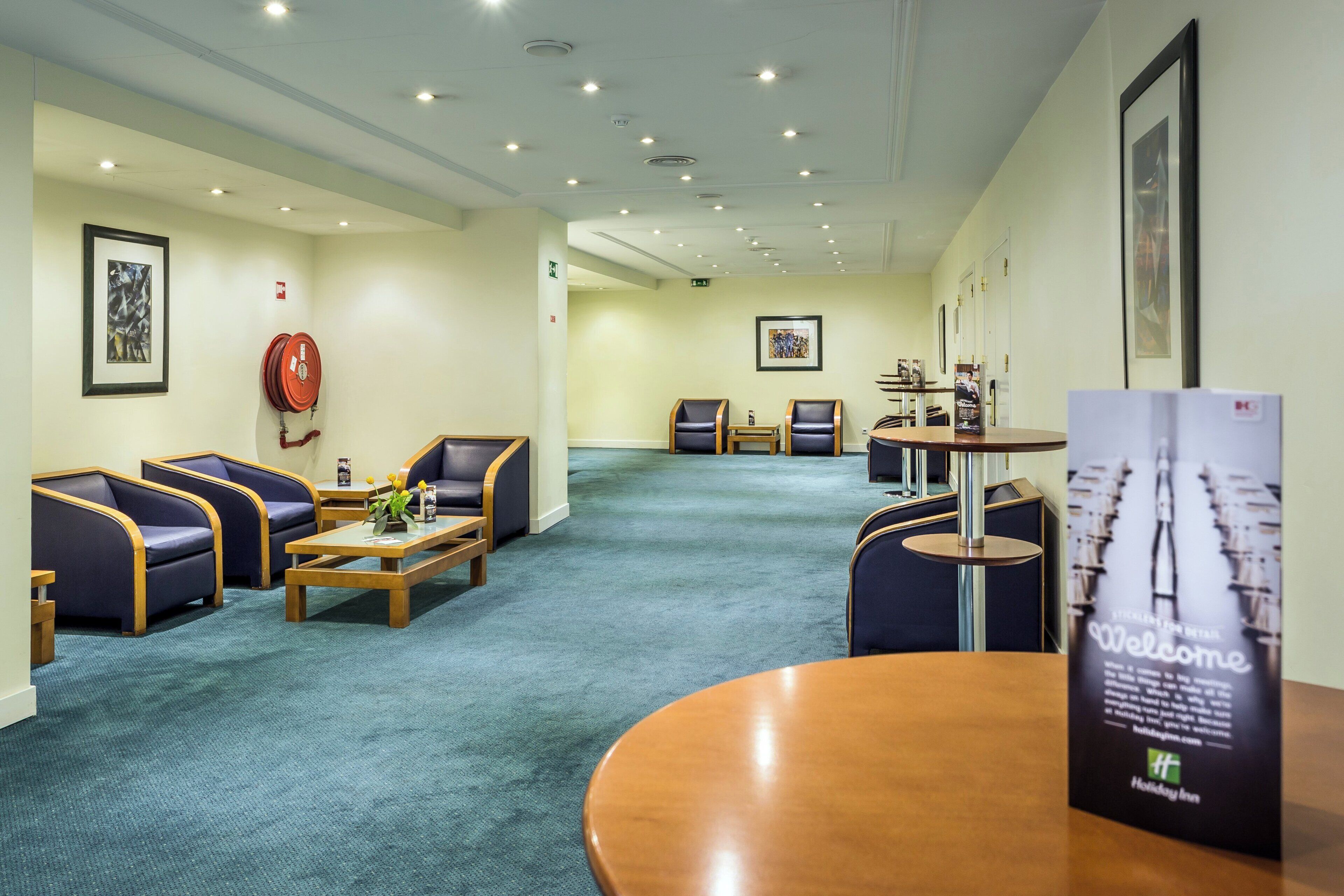 A hotel lobby with seating areas, a reception desk, and a fire extinguisher on the wall.