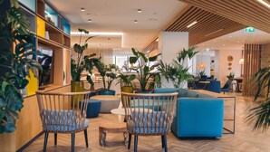 Eine moderne Hotelhalle mit Holzboden, blauen Sitzgelegenheiten und diversen Pflanzen.