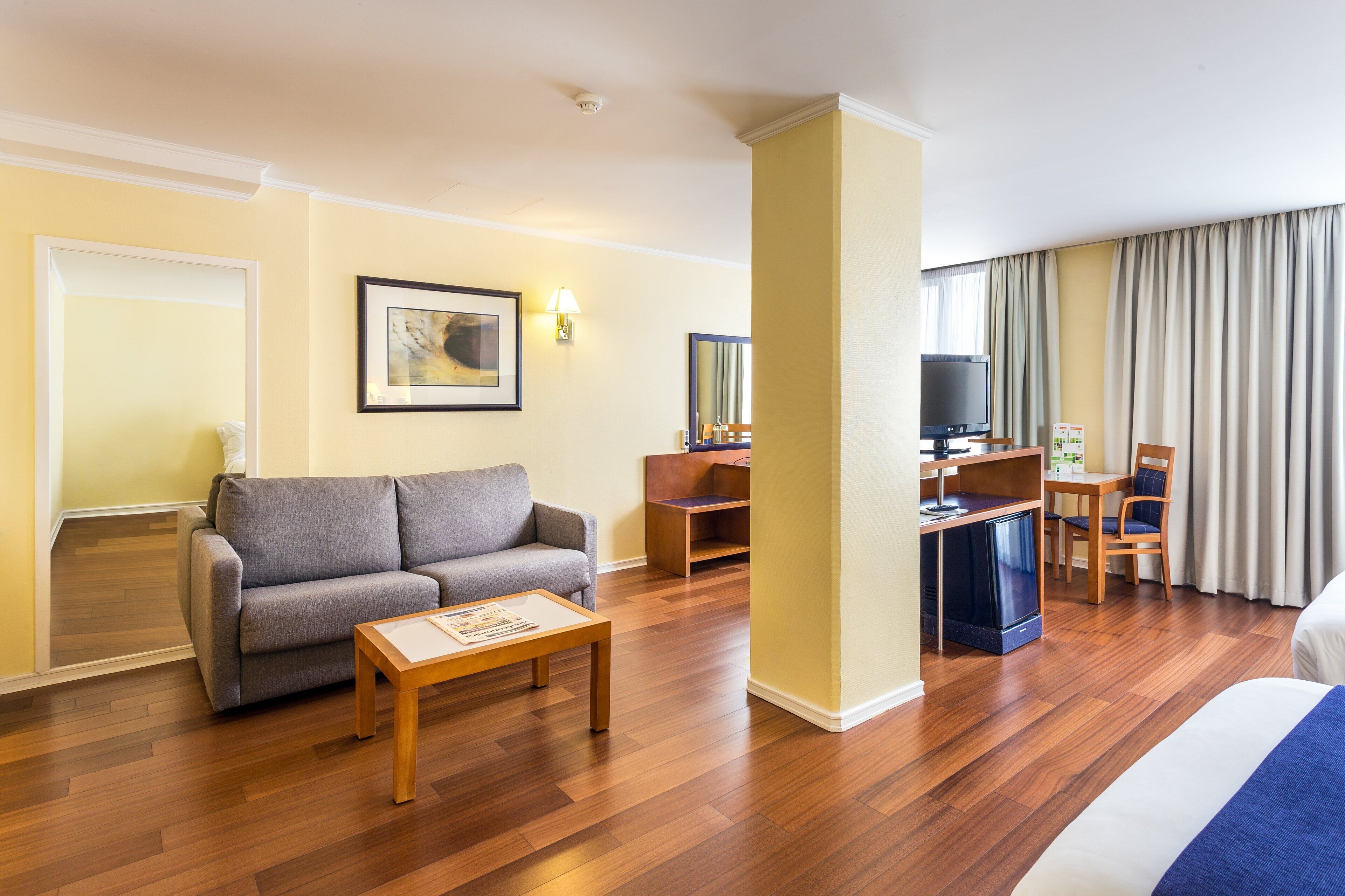 A hotel room with a sofa, a small table, a TV, a desk, and a bed.