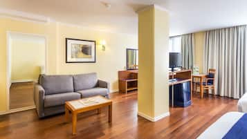 A hotel room with a sofa, a small table, a TV, a desk, and a bed.