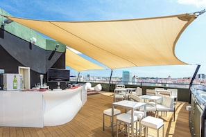 Un bar en la azotea con barra, zona de estar y una gran vela de sombra.