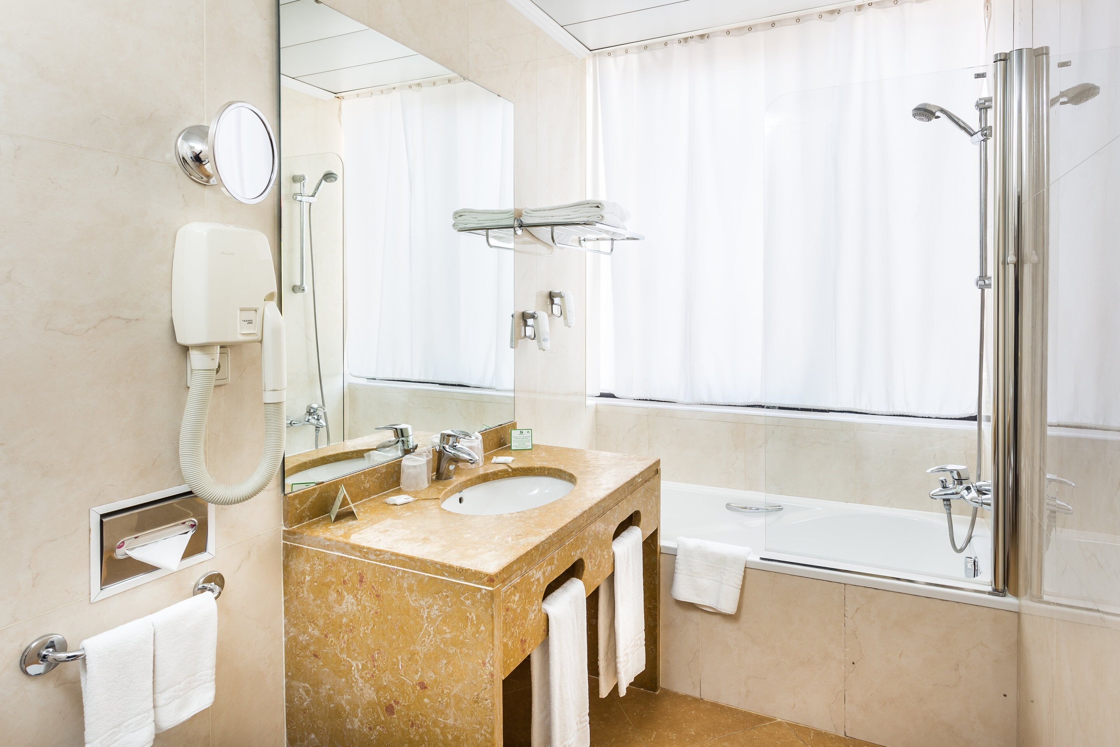 Ein modernes Badezimmer mit Marmorwaschbecken, einem großen Spiegel, einer Handbrause und einer Badewanne.