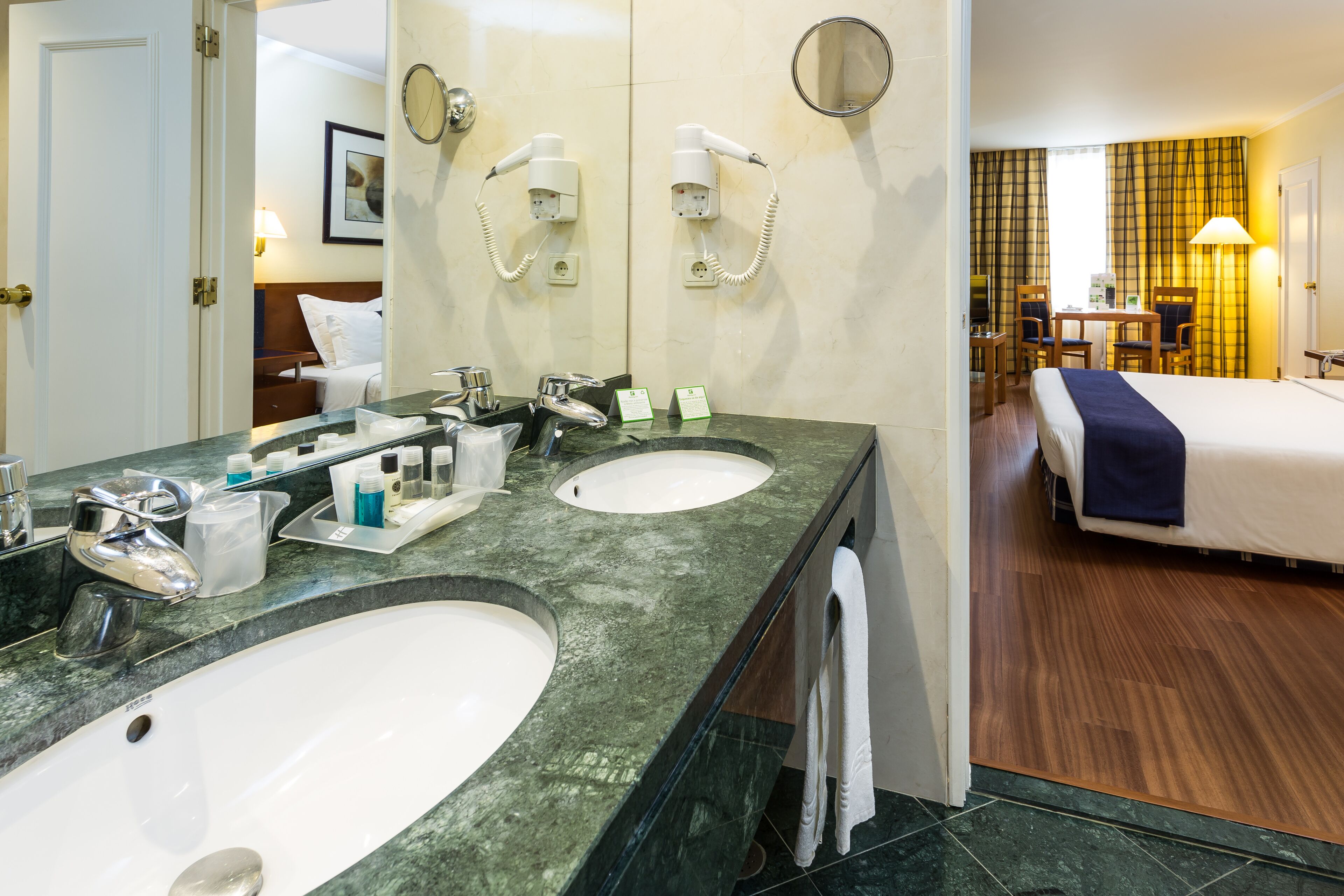 Un baño de hotel con dos lavamanos, un espejo y secadores de pelo.