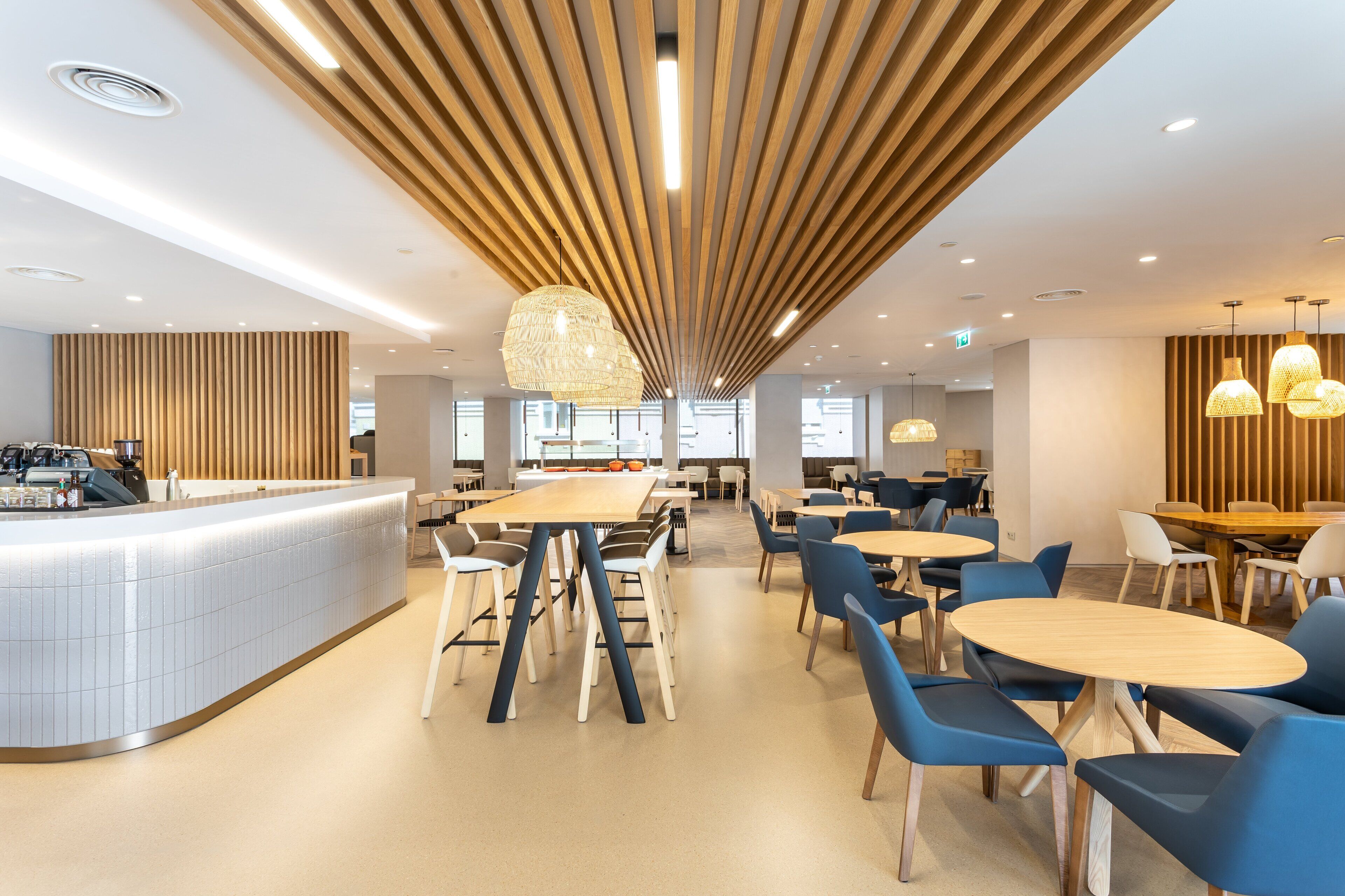 A modern restaurant with a long counter, multiple tables, and blue chairs.