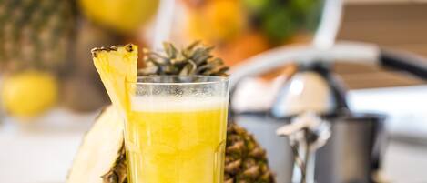 A glass of pineapple juice with a pineapple slice garnish, a whole pineapple, and a metal container in a kitchen setting.