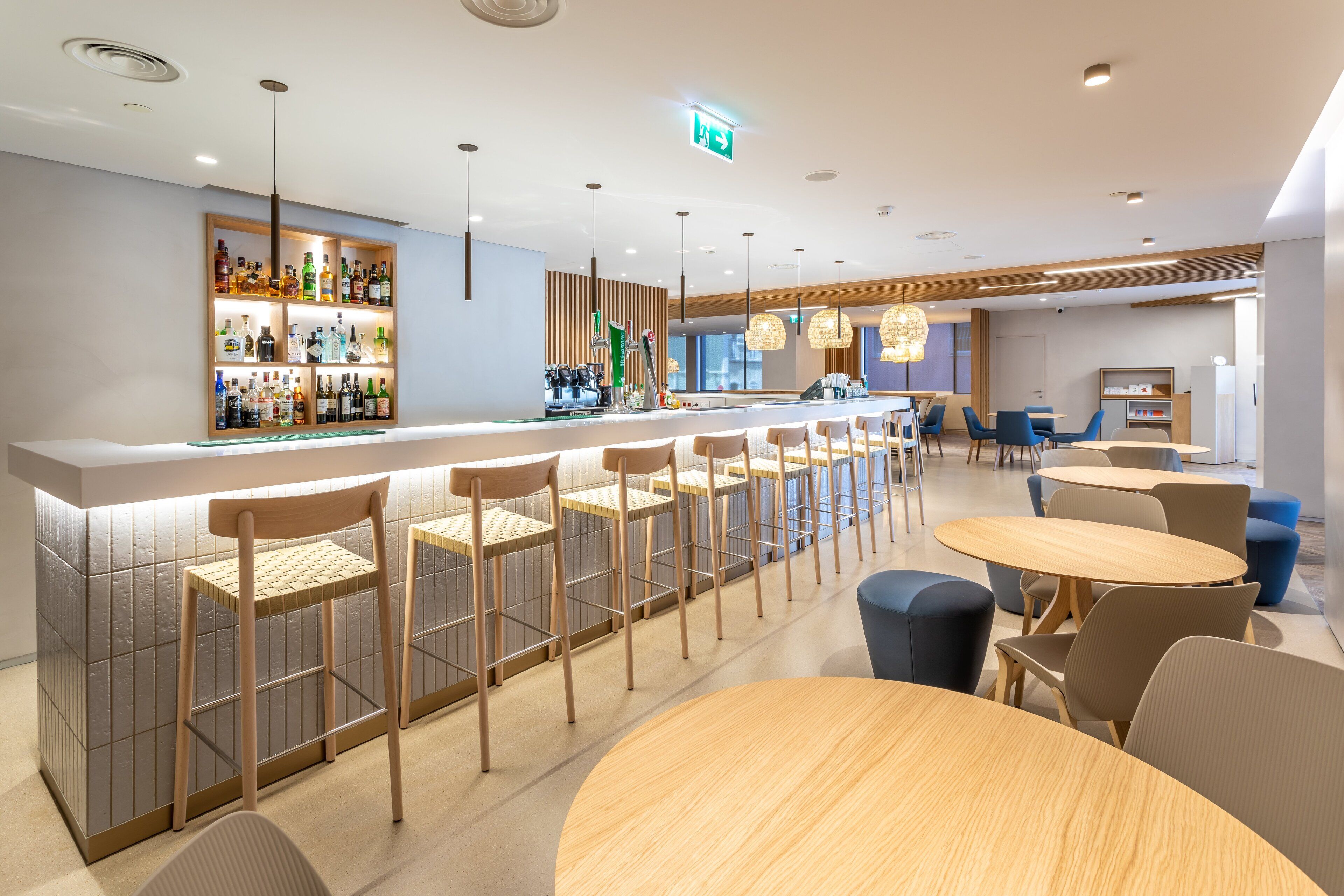 A modern bar area with a long counter, bar stools, and round tables.