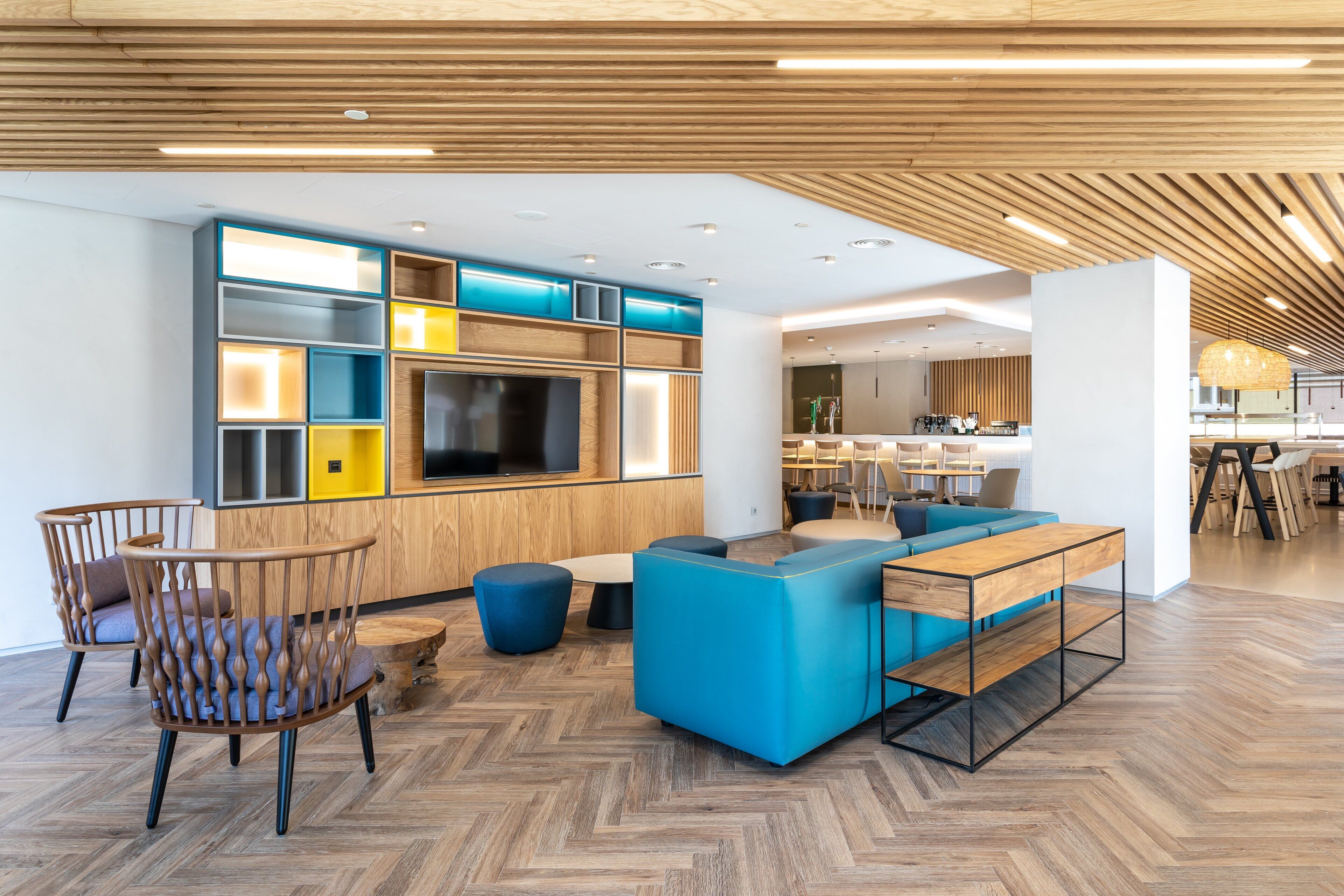 A modern interior with a wooden ceiling, a TV mounted on a wall, a blue sofa, and a wooden dining table.