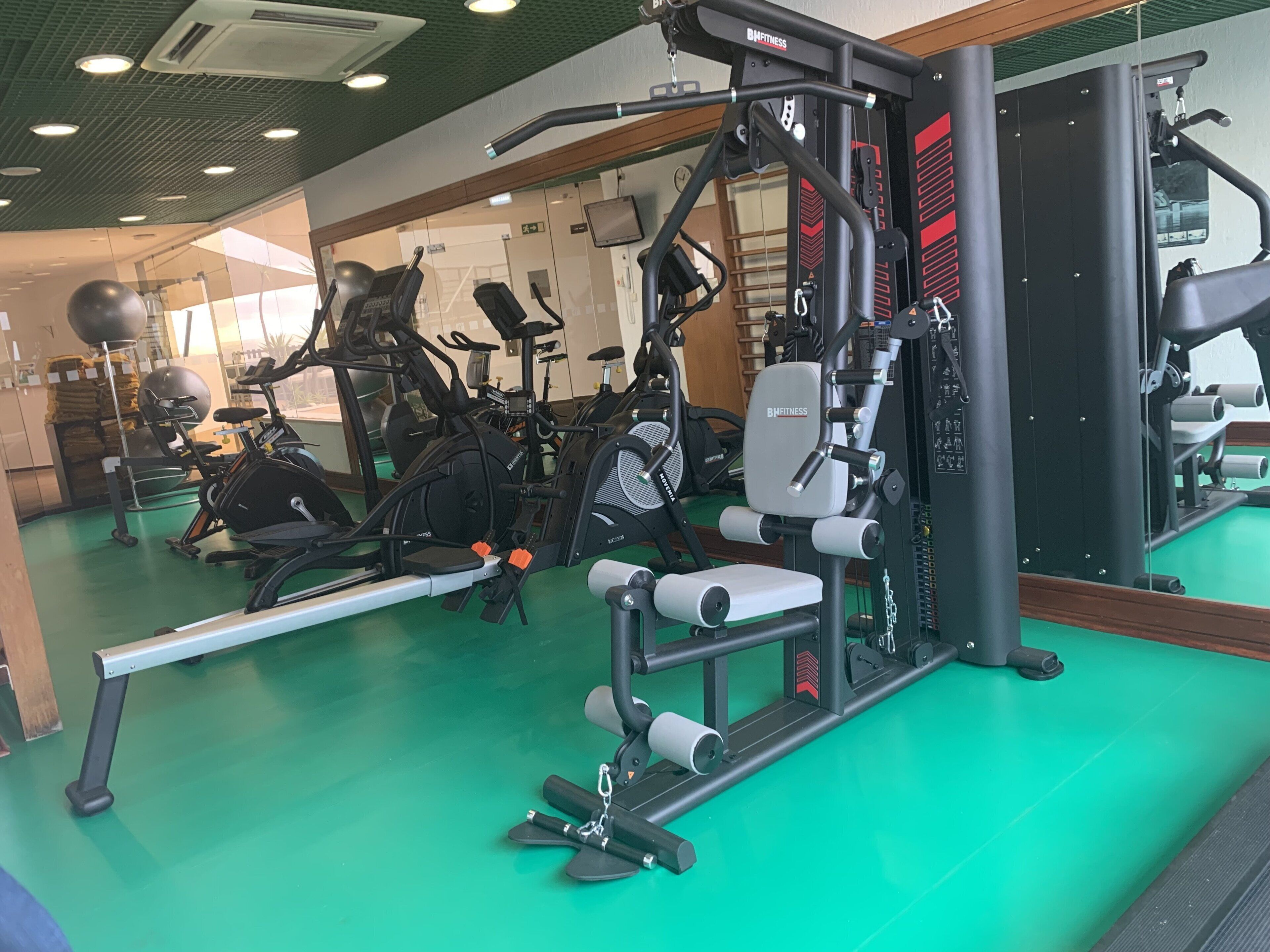 Een fitnessruimte met diverse trainingsapparaten, waaronder loopbanden, hometrainers en krachtapparaten.