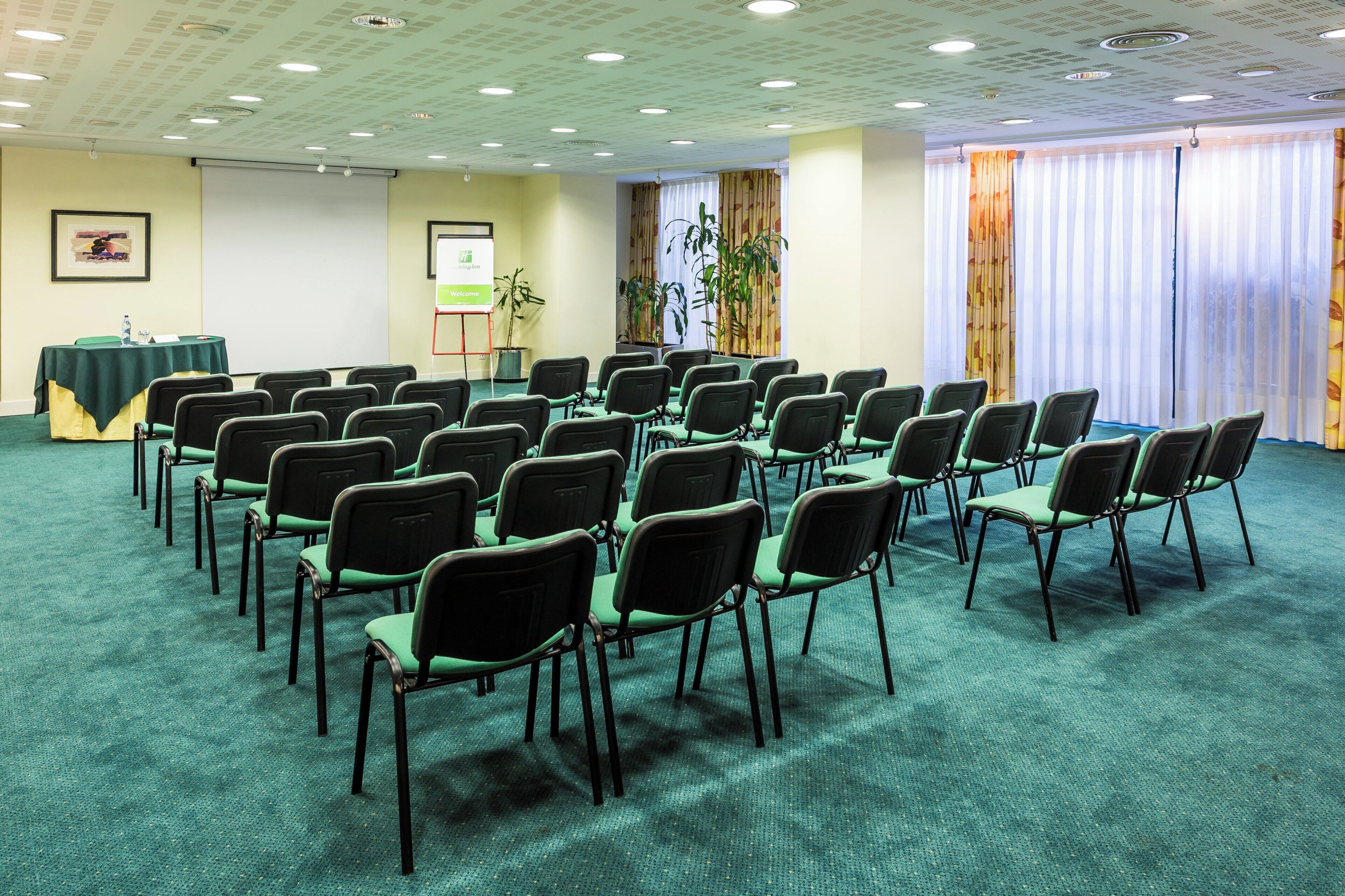 A conference room with rows of chairs, a projector screen, and a welcome sign.