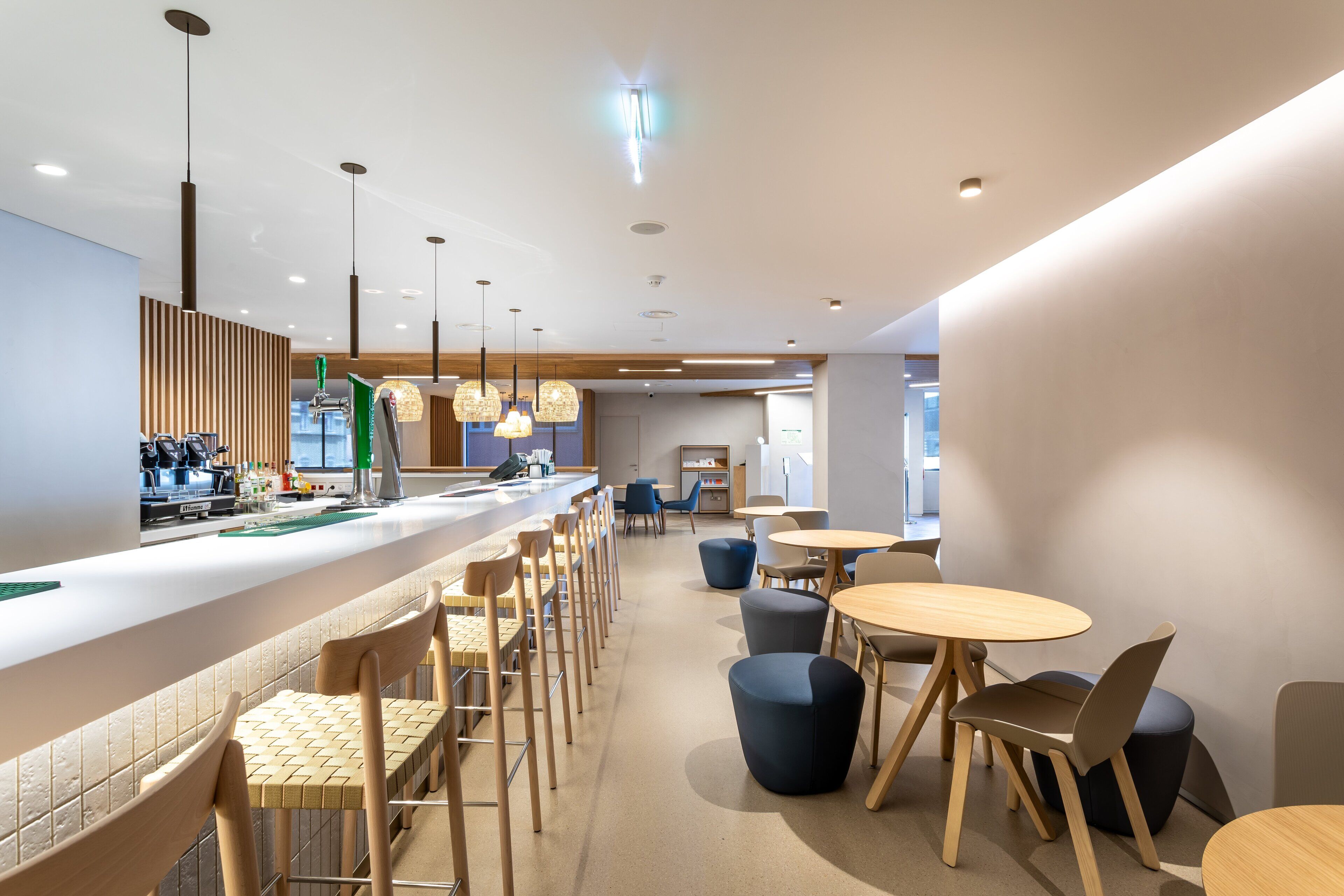 A modern cafe with a long counter, barista station, and seating area with round tables and chairs.