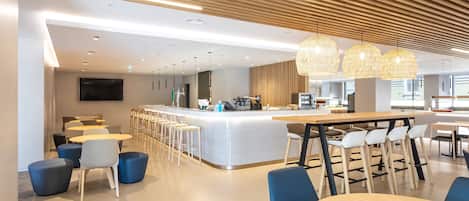 A modern hotel lobby with a central bar area, seating arrangements, and a wooden ceiling design.