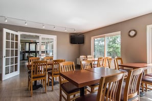 A dining area with wooden tables and chairs, a flat-screen TV mounted on the wall, and large windows allowing natural light. - Comfort Inn (Huntsville)