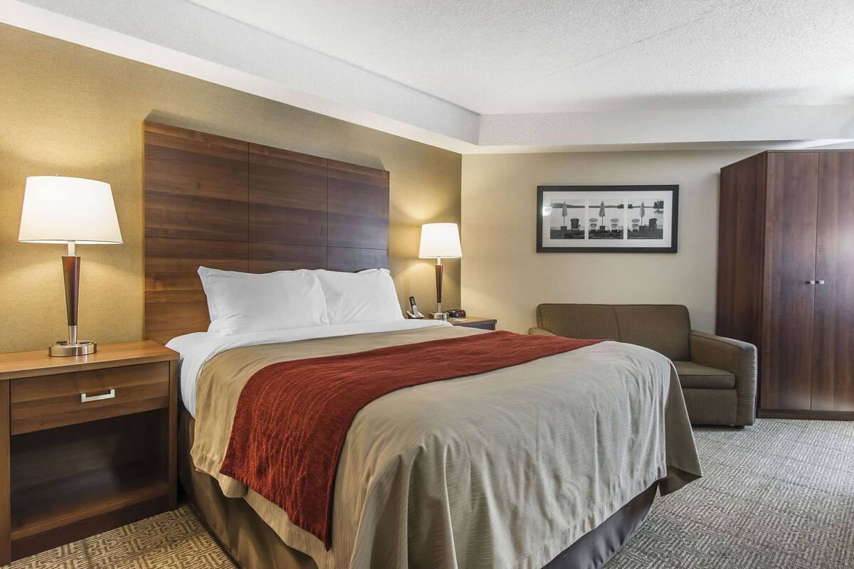 Habitación de hotel con cama, dos mesitas de noche con lámparas, una silla, armario y un cuadro en la pared.