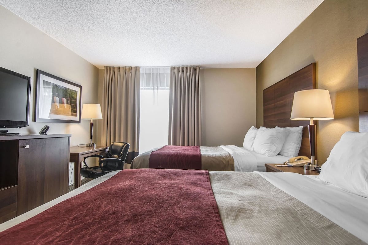 A hotel room with two beds, a desk, a TV, and a window with curtains.