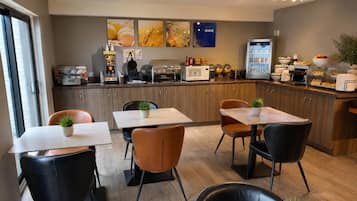 Un comedor moderno con mesas y sillas, una cafetera, un refrigerador y una exhibición de frutas.