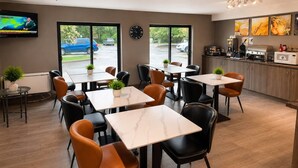Un restaurant doté de plusieurs tables et chaises, d’un espace cuisine et d’un téléviseur diffusant une chaîne d’information.