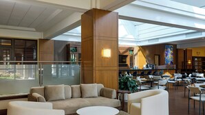 A spacious lobby with a high ceiling, a central wooden column, a seating area with sofas and chairs, and a view of the kitchen area in the background. - Detroit Marriott Troy (Troy)