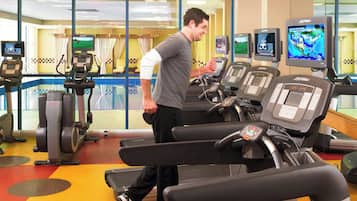 Un gimnasio con cintas de correr, bicicletas estáticas y una zona de piscina visible a través de las puertas de cristal.