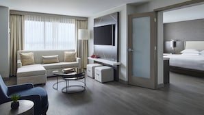 A modern hotel room with a sofa, armchair, and a TV mounted on the wall. - Detroit Marriott Troy (Troy)