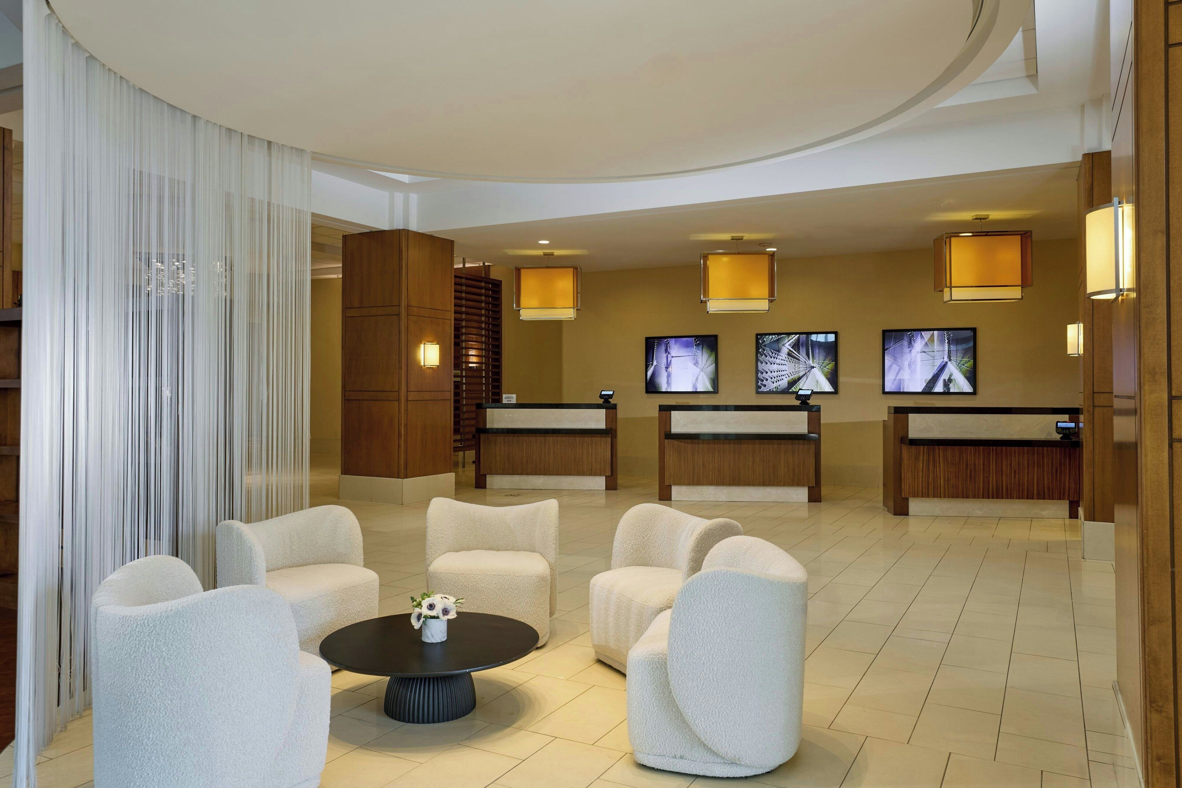 A hotel lobby with plush seating, a reception desk, and wall-mounted televisions.