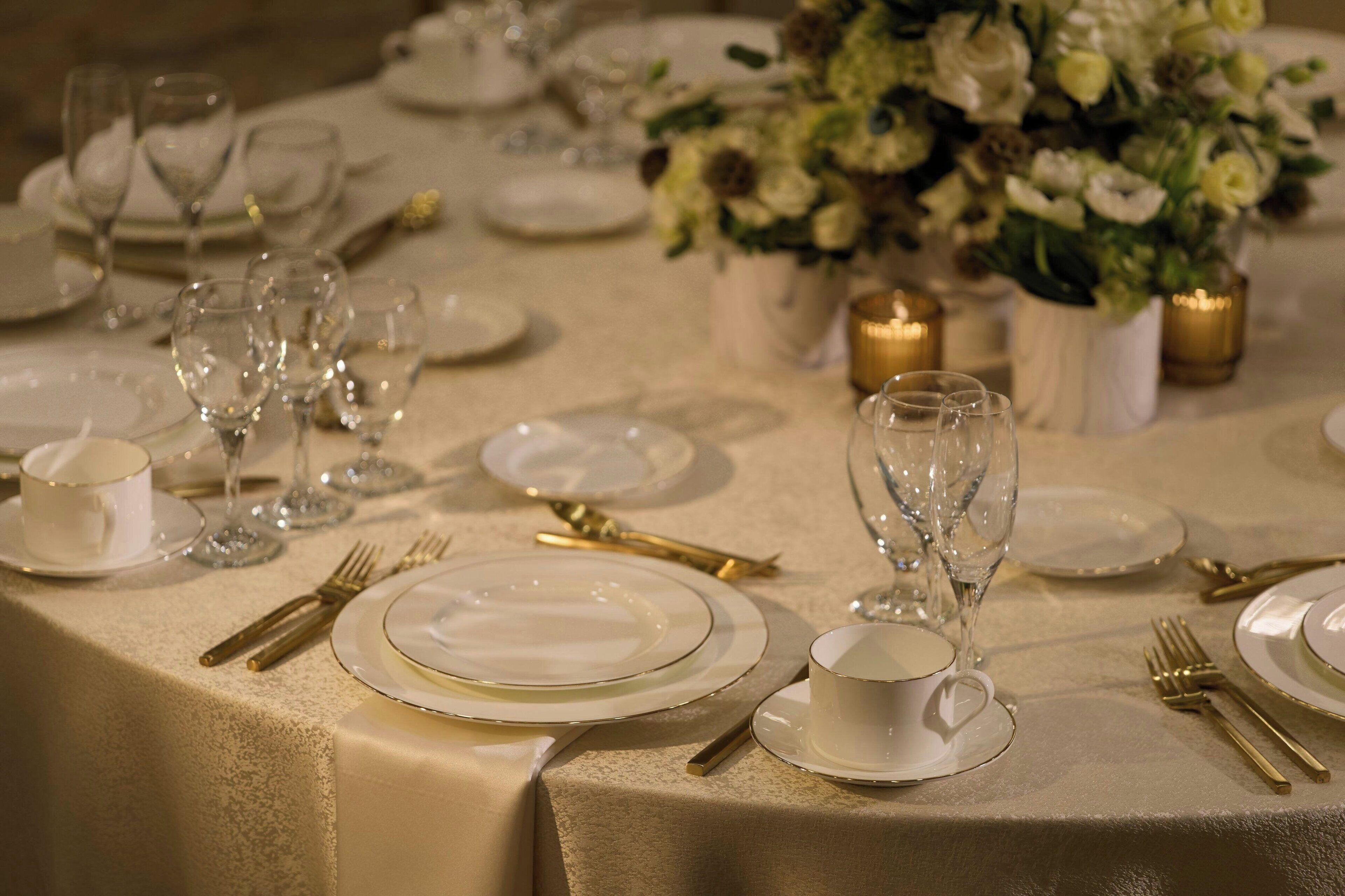 A table set for a formal dining occasion with white plates, gold cutlery, and clear glassware.