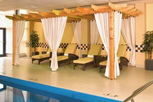 Zona de piscina con sillones de descanso, una pérgola de madera y suelo de baldosas.