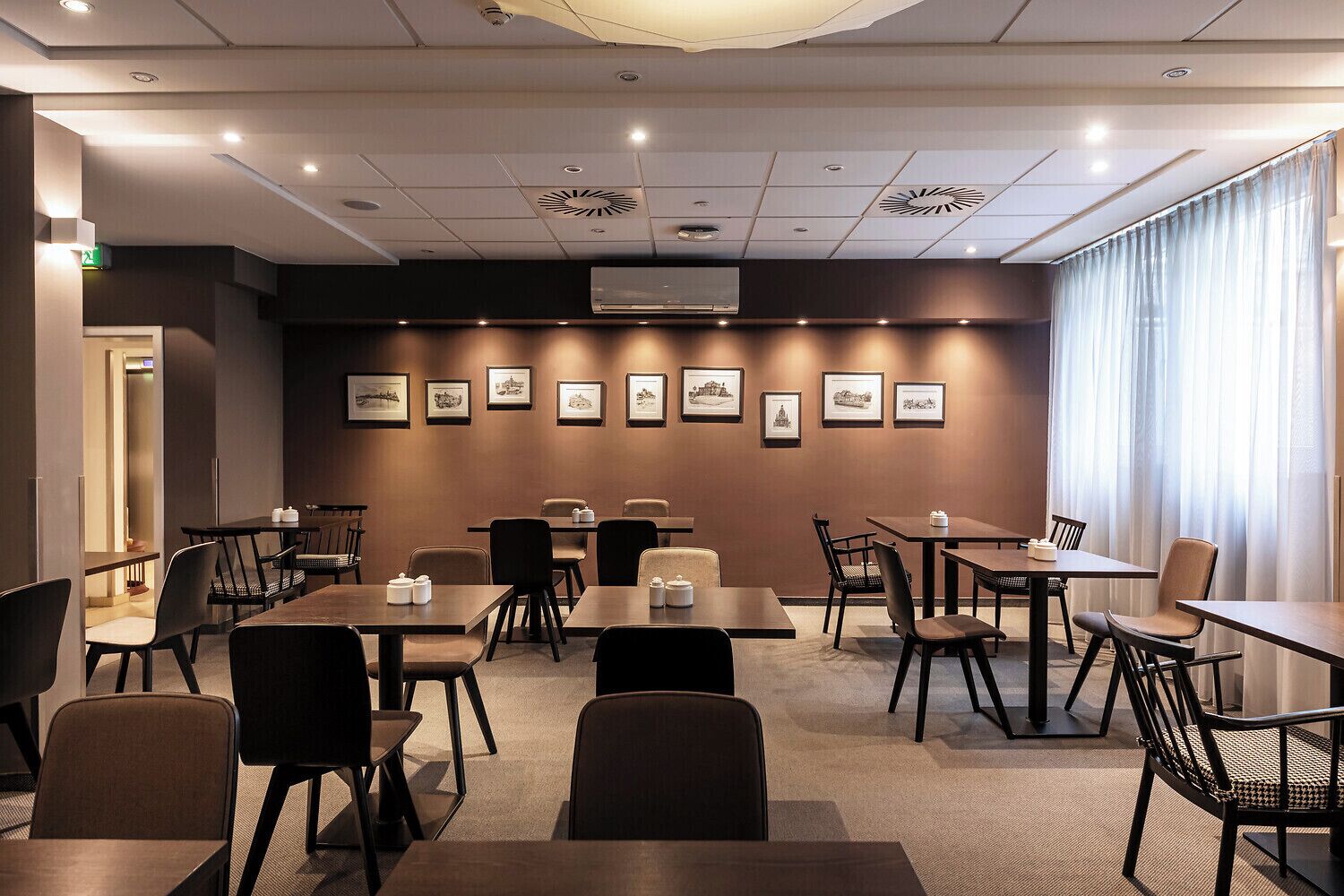 Ein Konferenzraum mit Tischen und Stühlen, Bilder an der Wand und ein großes Fenster mit Vorhängen.