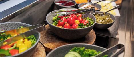 Un bufé con diversos platos, incluyendo un tazón de ensalada con tomates y pepinos.