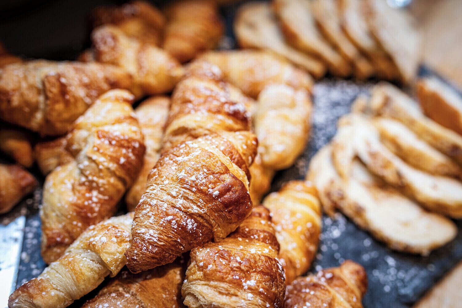 Variedad de pasteles, incluyendo croissants y otras delicias horneadas, sobre una superficie de pizarra.