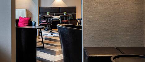 A modern interior with a geometric patterned floor, a seating area with black chairs, and a dining setup with a black table and chairs.