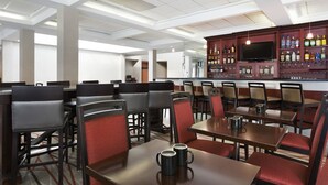 A hotel dining area with multiple tables and chairs, a bar with liquor bottles, and a television screen. - Radisson Hotel Akron/Fairlawn (Akron)
