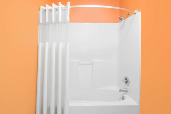 A white shower enclosure with a showerhead and a control panel against an orange wall. - Howard Johnson by Wyndham Dothan (Dothan)