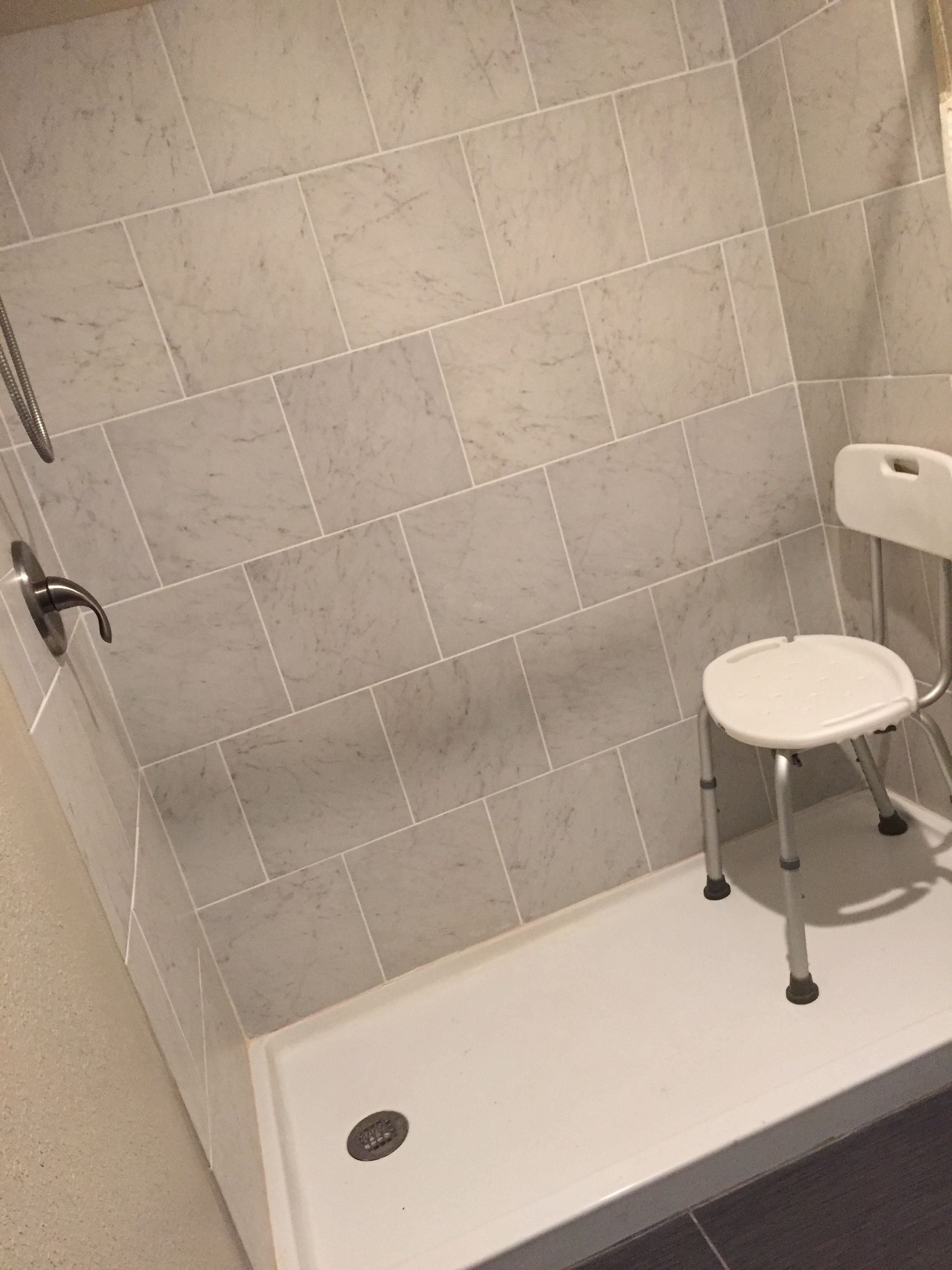 Un bagno con zona doccia, una sedia bianca e una barra di sostegno.