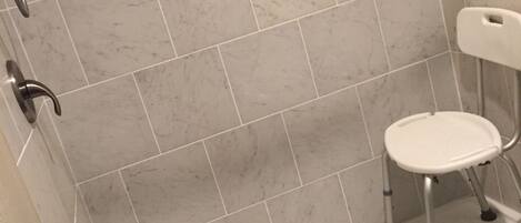 Un bagno con zona doccia, una sedia bianca e una barra di sostegno.
