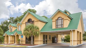 Un hotel con techo verde y paredes amarillas, que cuenta con una entrada cubierta y señal de acceso para personas con discapacidad.