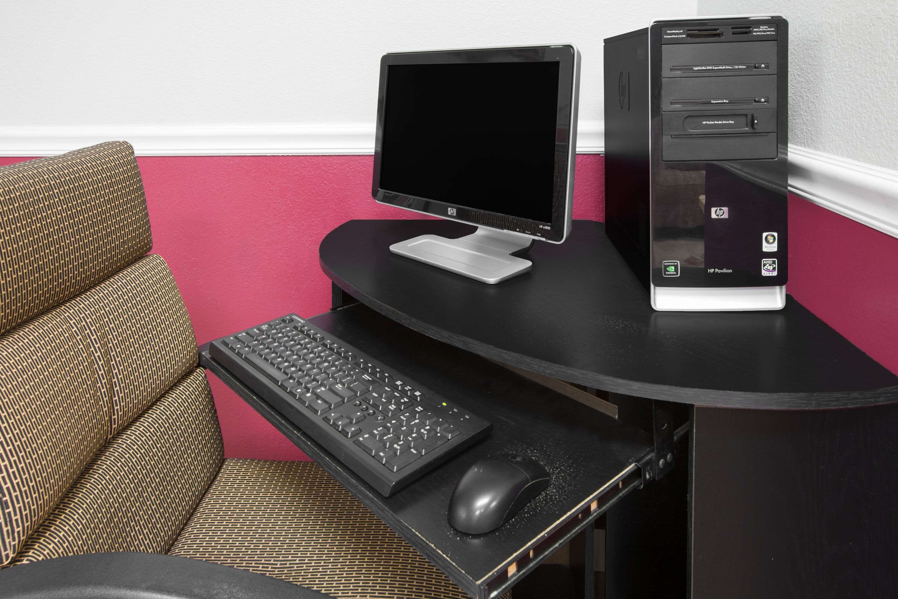 Un espace de travail compact, comprenant un ordinateur de bureau, un clavier et une souris, installé sur un bureau noir.