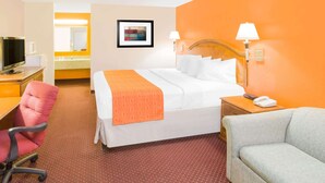 Habitación de hotel con cama, escritorio con computadora, silla, mesita de noche con lámpara y teléfono.