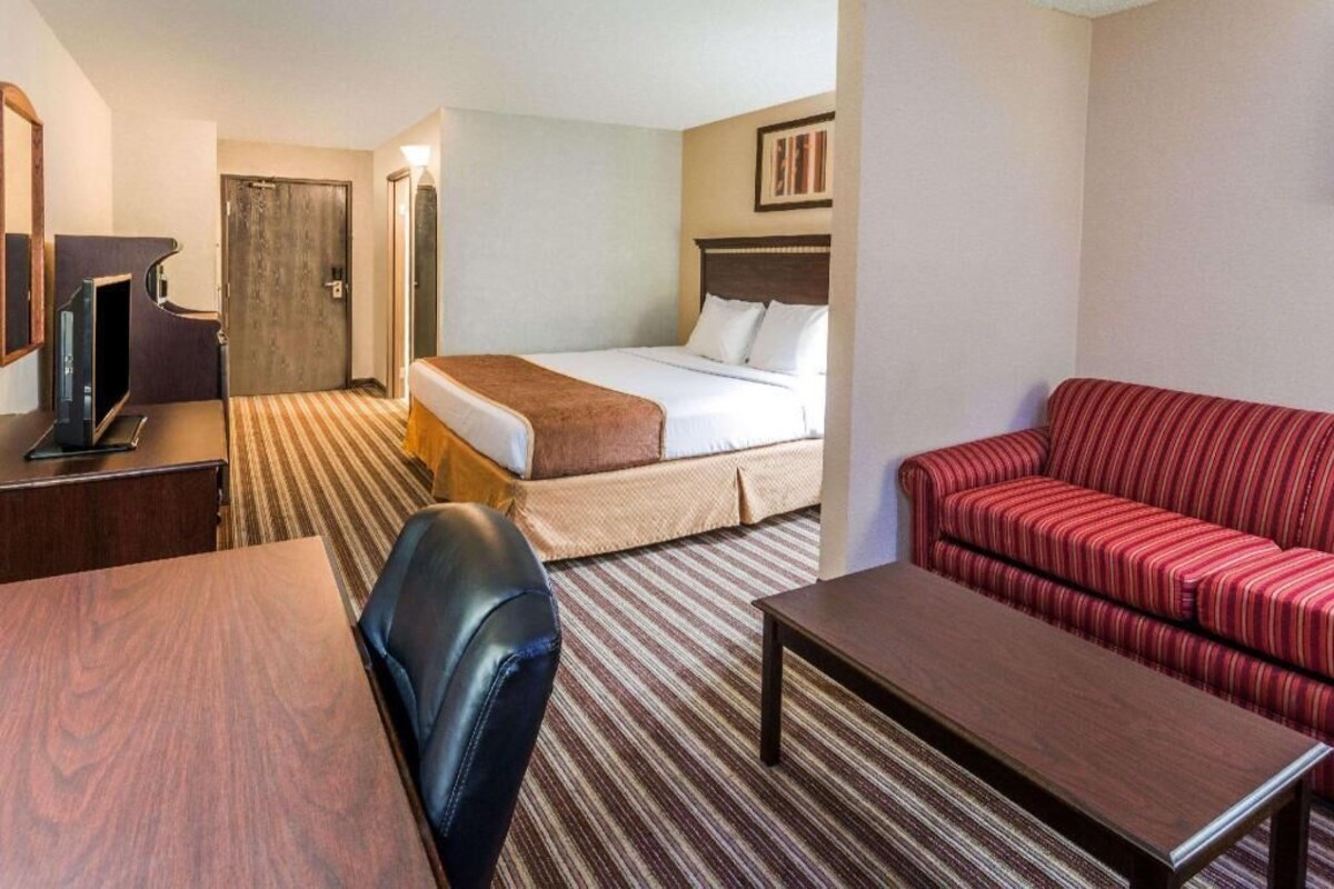 A hotel room with a bed, a red-striped sofa, a wooden table, a TV, and a desk with a chair.