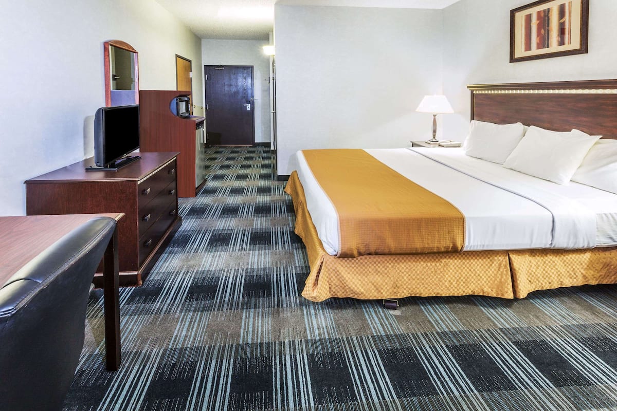 Una habitación de hotel con cama, escritorio, silla, televisor y puerta de baño.