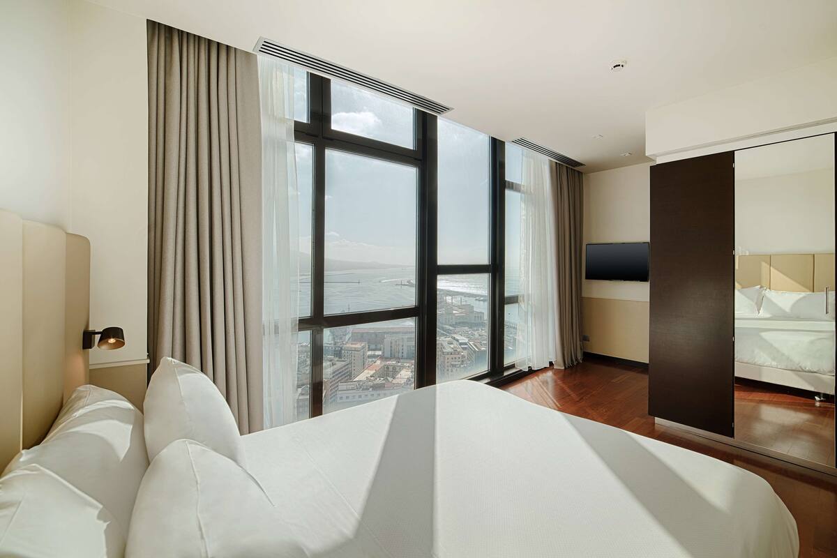 A hotel room with a large window, a bed, a TV, and a wardrobe.