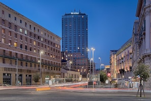A high-rise hotel with multiple floors, a prominent 'TH HOTELS' sign, and a busy street with light trails indicating traffic.