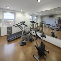 Una palestra con attrezzature per esercizi, un grande specchio e una finestra vista città.