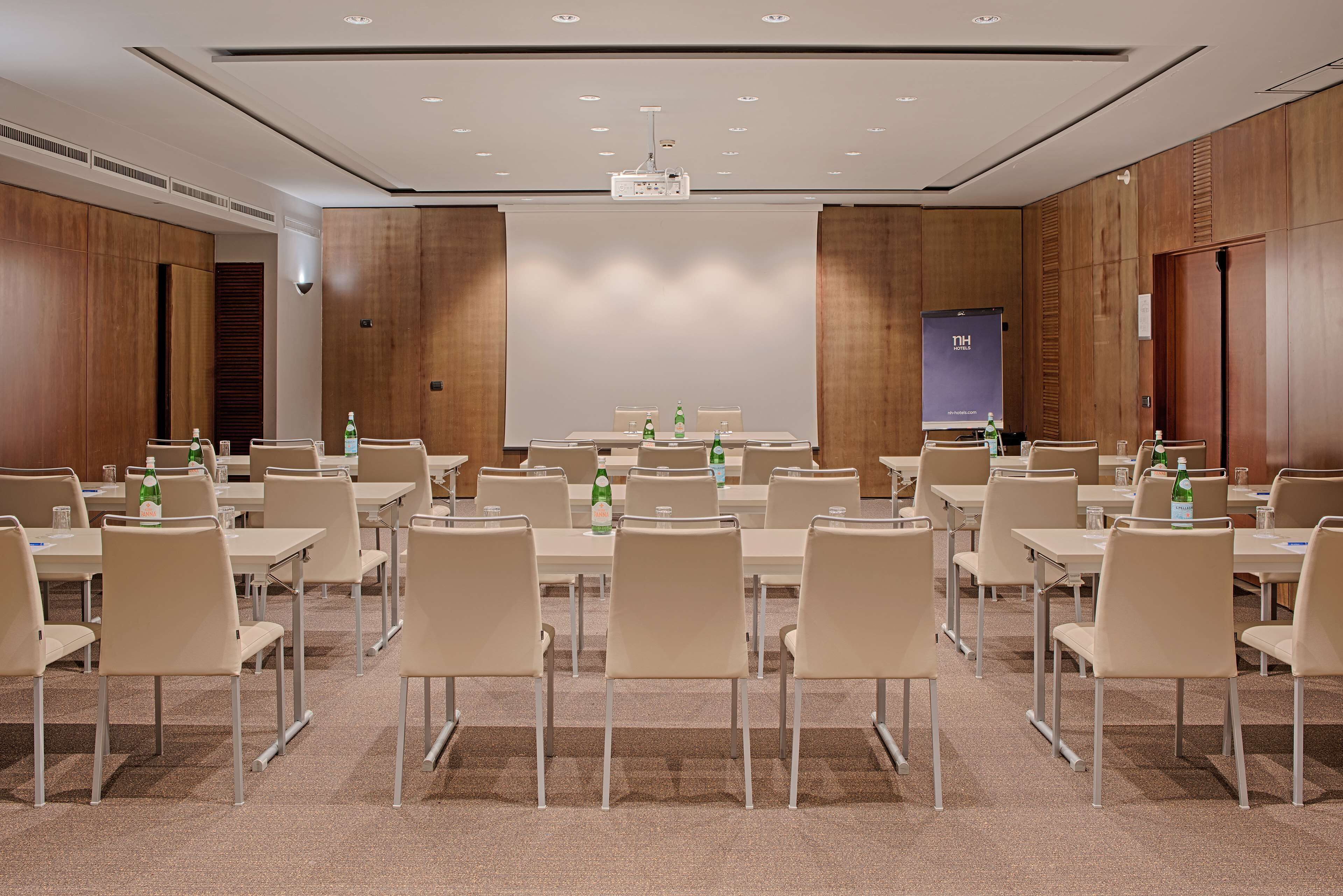 A conference room with multiple tables and chairs, equipped with projectors and screens.
